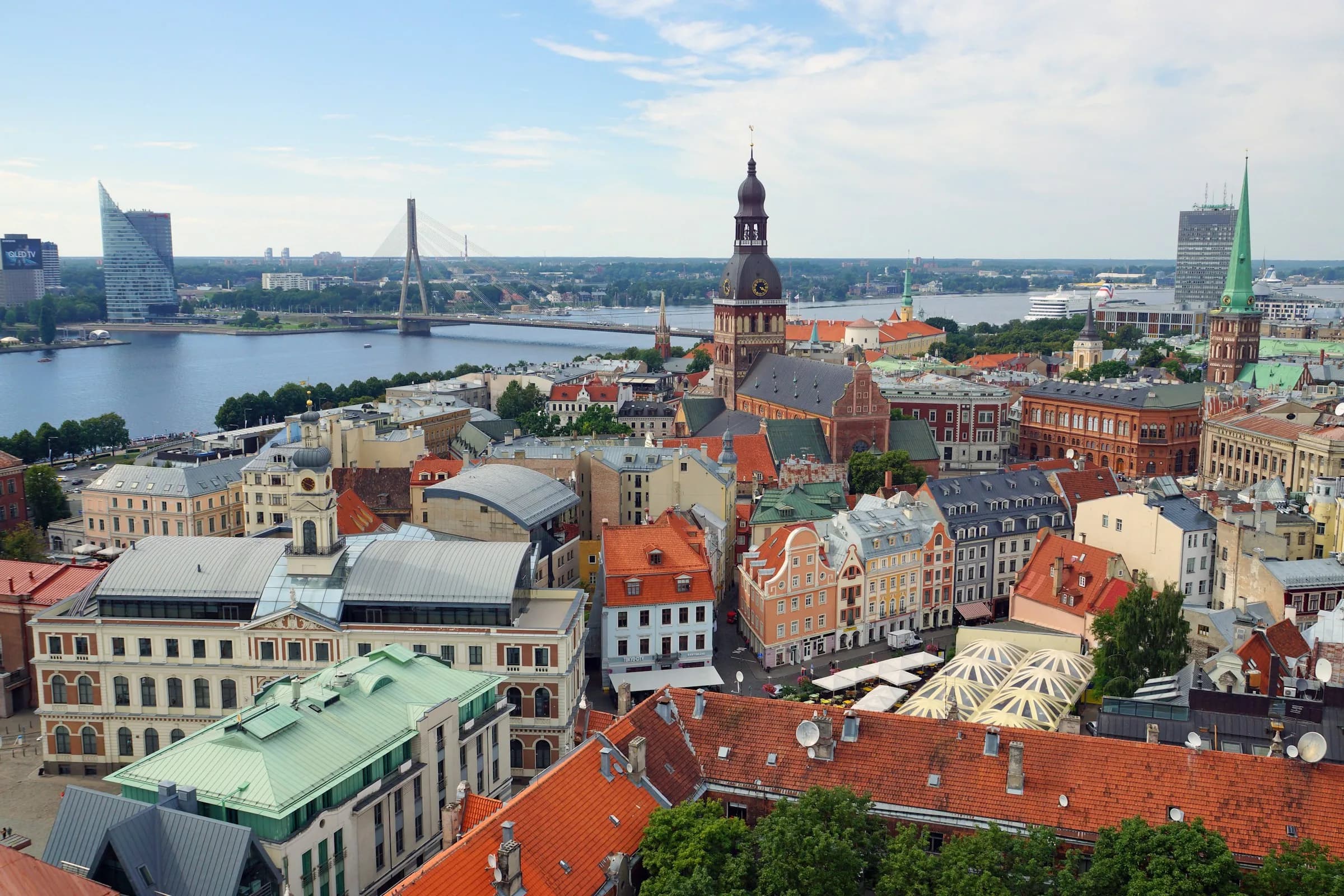 The red roofs of Riga's old town in Latvia, with a church tower, the Daugava River and a cable-stayed bridge beyond.