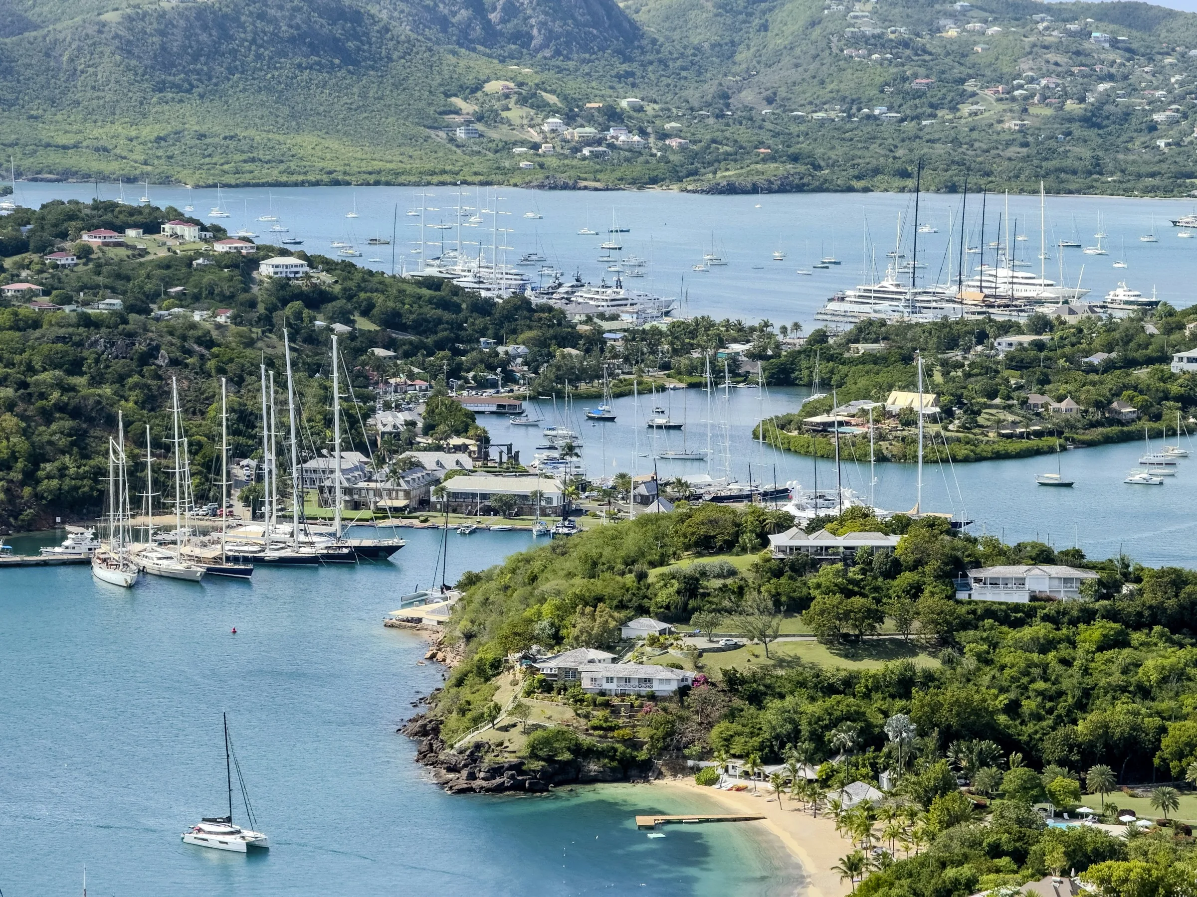 Veleros amarrados en English Harbour, Antigua, con Falmouth Harbour y colinas verdes al fondo.