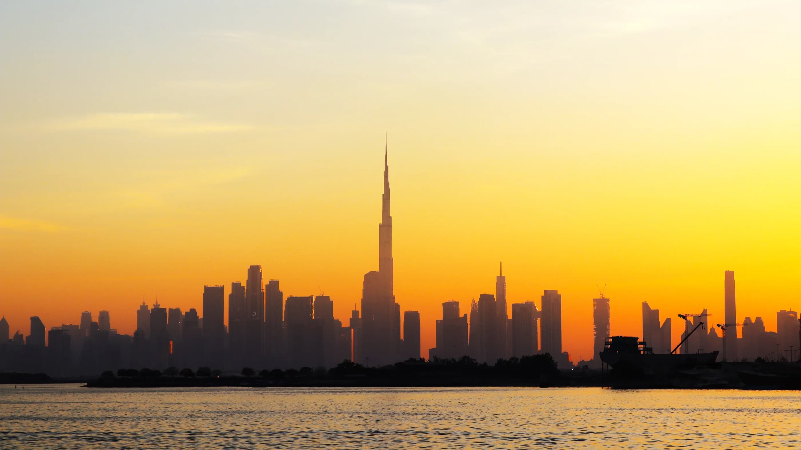 Vista del horizonte de Dubái y del Burj Khalifa sobre el agua desde Dubai Creek Harbour, al atardecer.