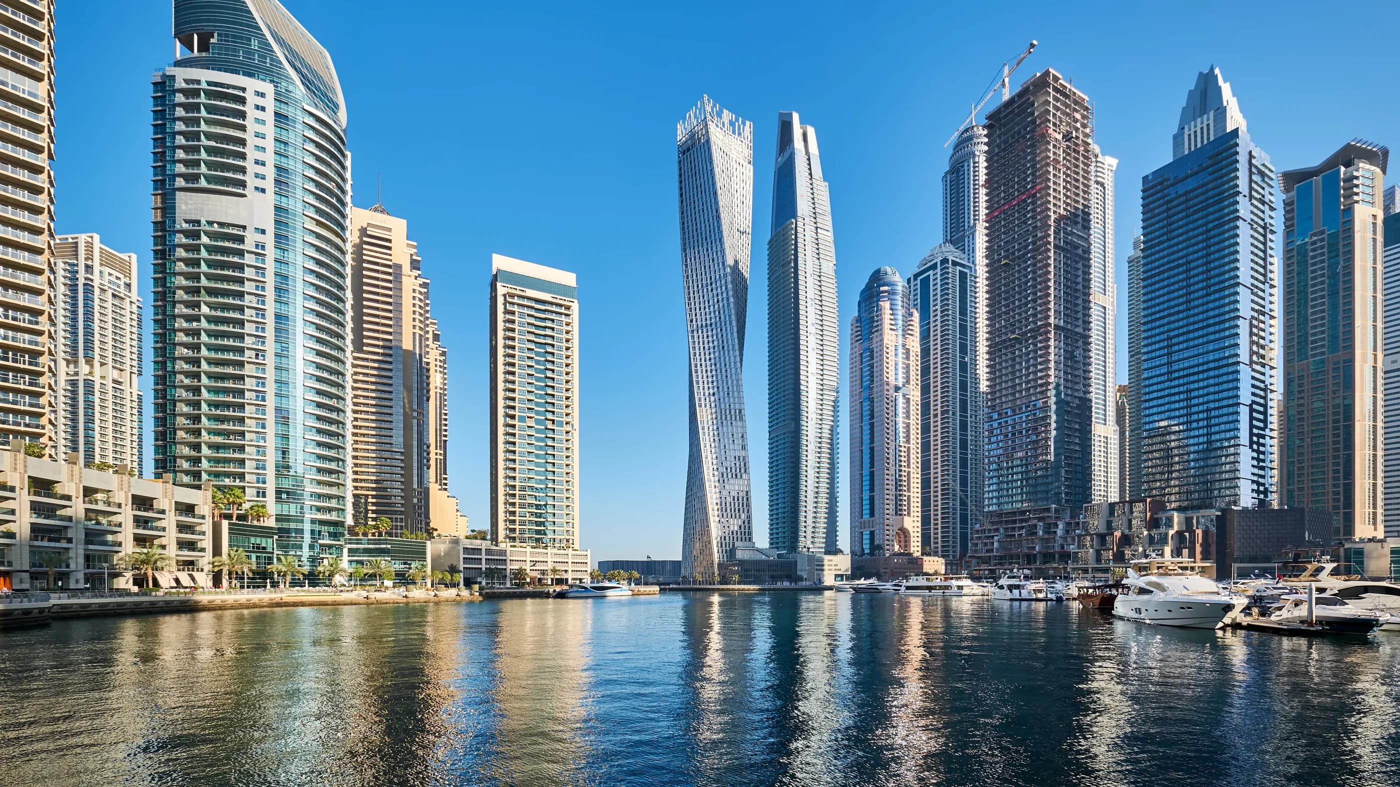 Torres residenciales a lo largo de Dubai Marina, reflejadas en el agua del puerto deportivo en un día despejado.